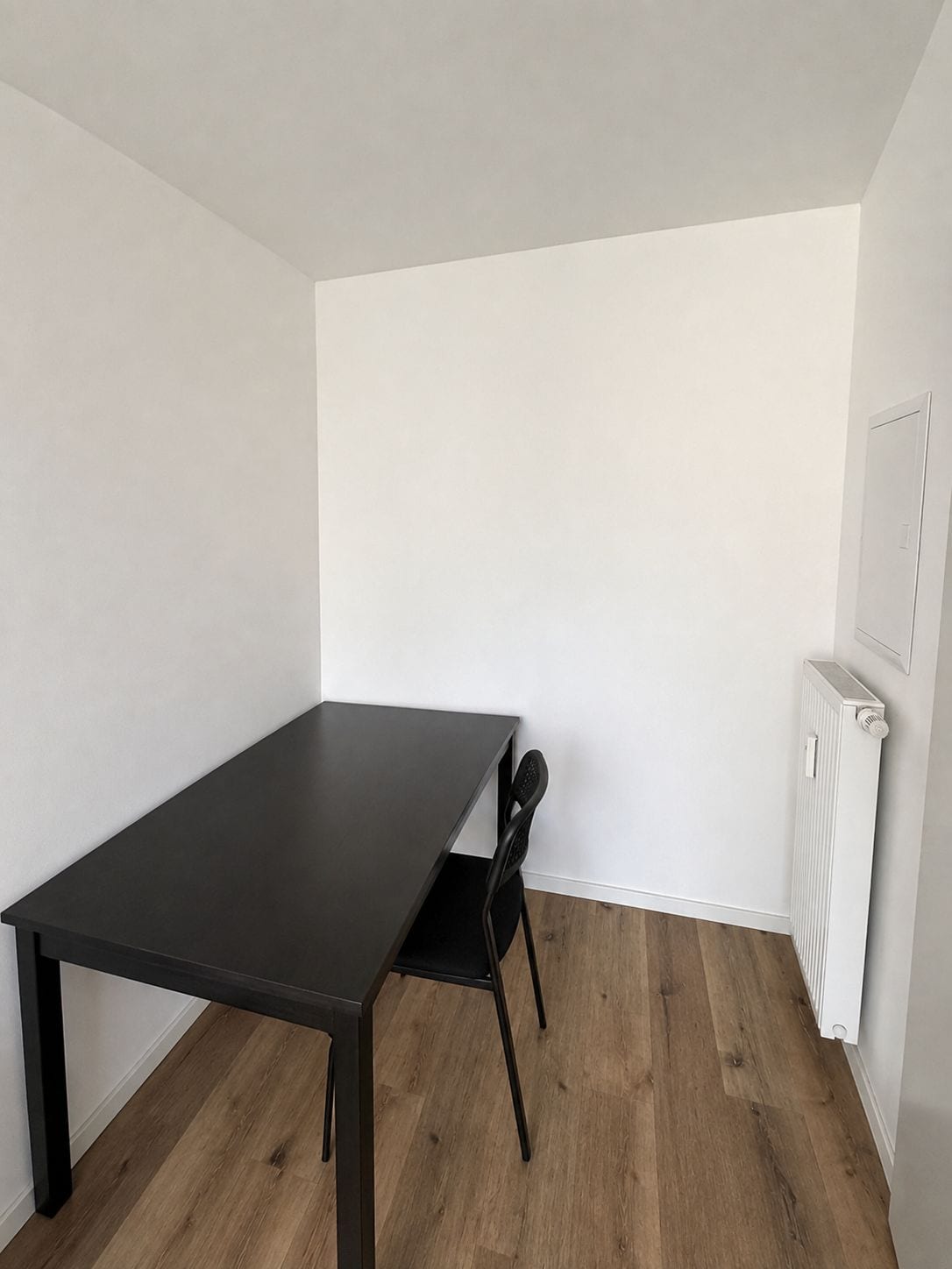 Ein Zimmer mit einem dunklen Holztisch und einem einzelnen schwarzen Stuhl.