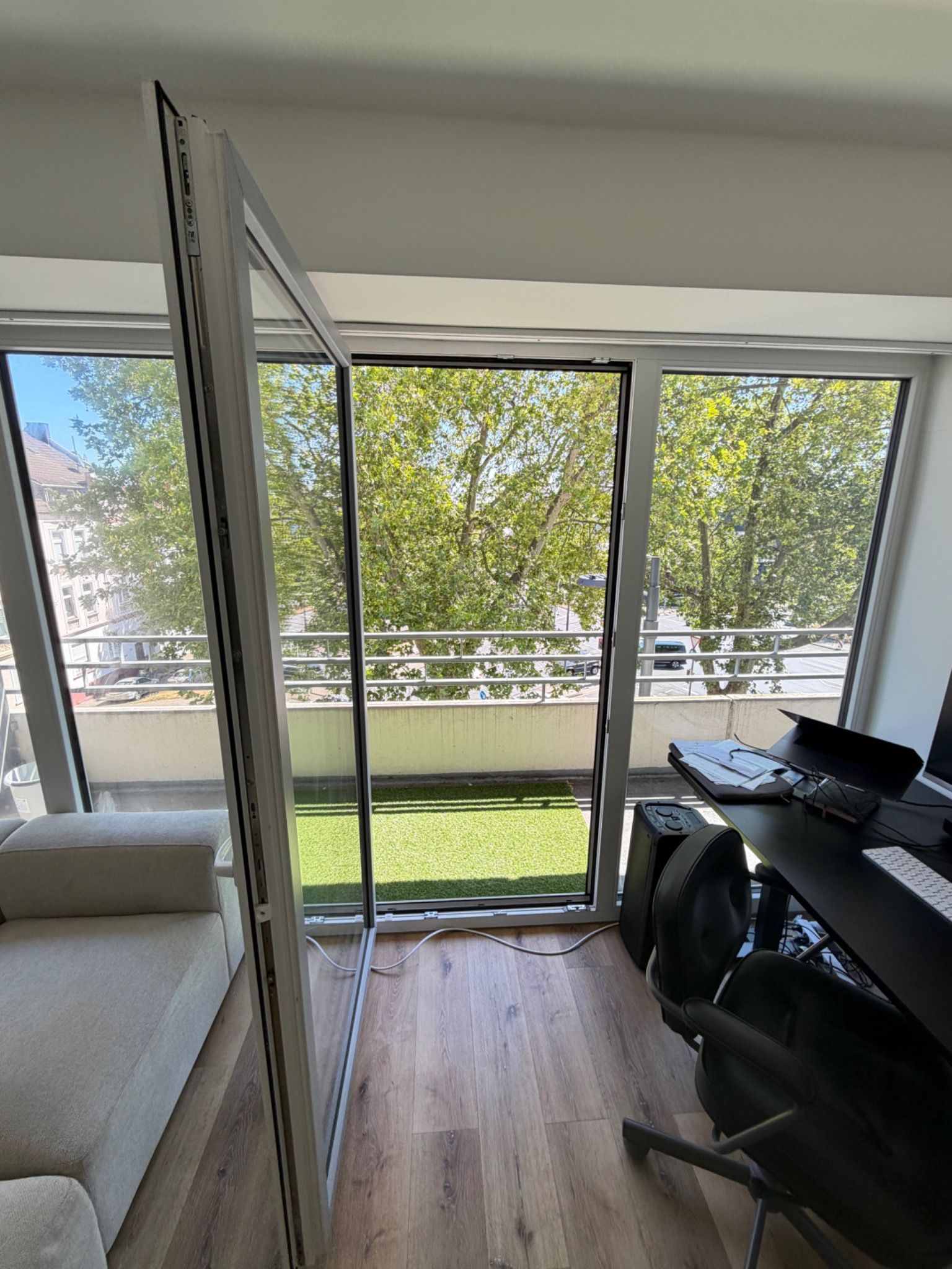 A room with a sliding glass door leading to a balcony with a view of trees and a grassy area.