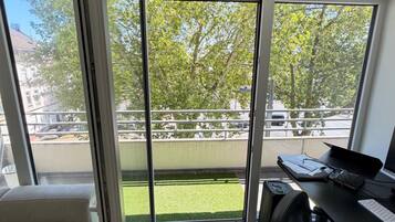 Ein Zimmer mit einer Schiebetür zu einem Balkon mit Blick auf Bäume und eine Rasenfläche.