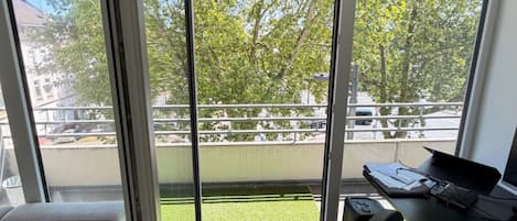 A room with a sliding glass door leading to a balcony with a view of trees and a grassy area.