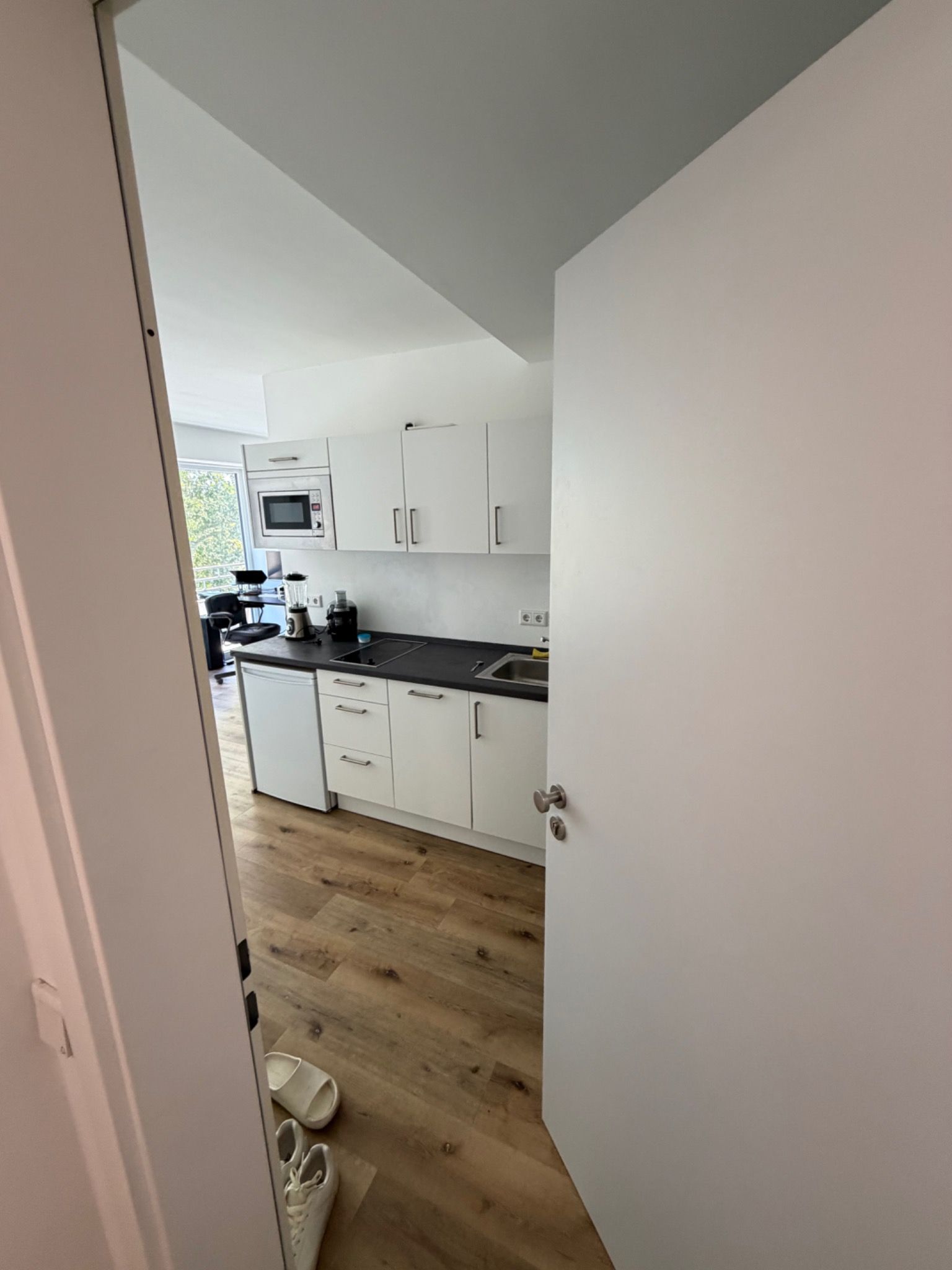 Eine moderne Küche mit weißen Schränken, einer schwarzen Arbeitsplatte und Holzboden.