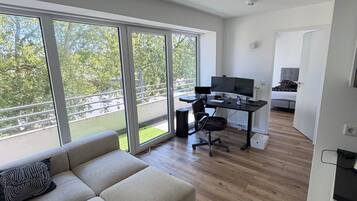 Ein modernes Wohnzimmer mit einer Couch, einem Schreibtisch mit einem Computer und großen Fenstern mit Blick ins Freie.