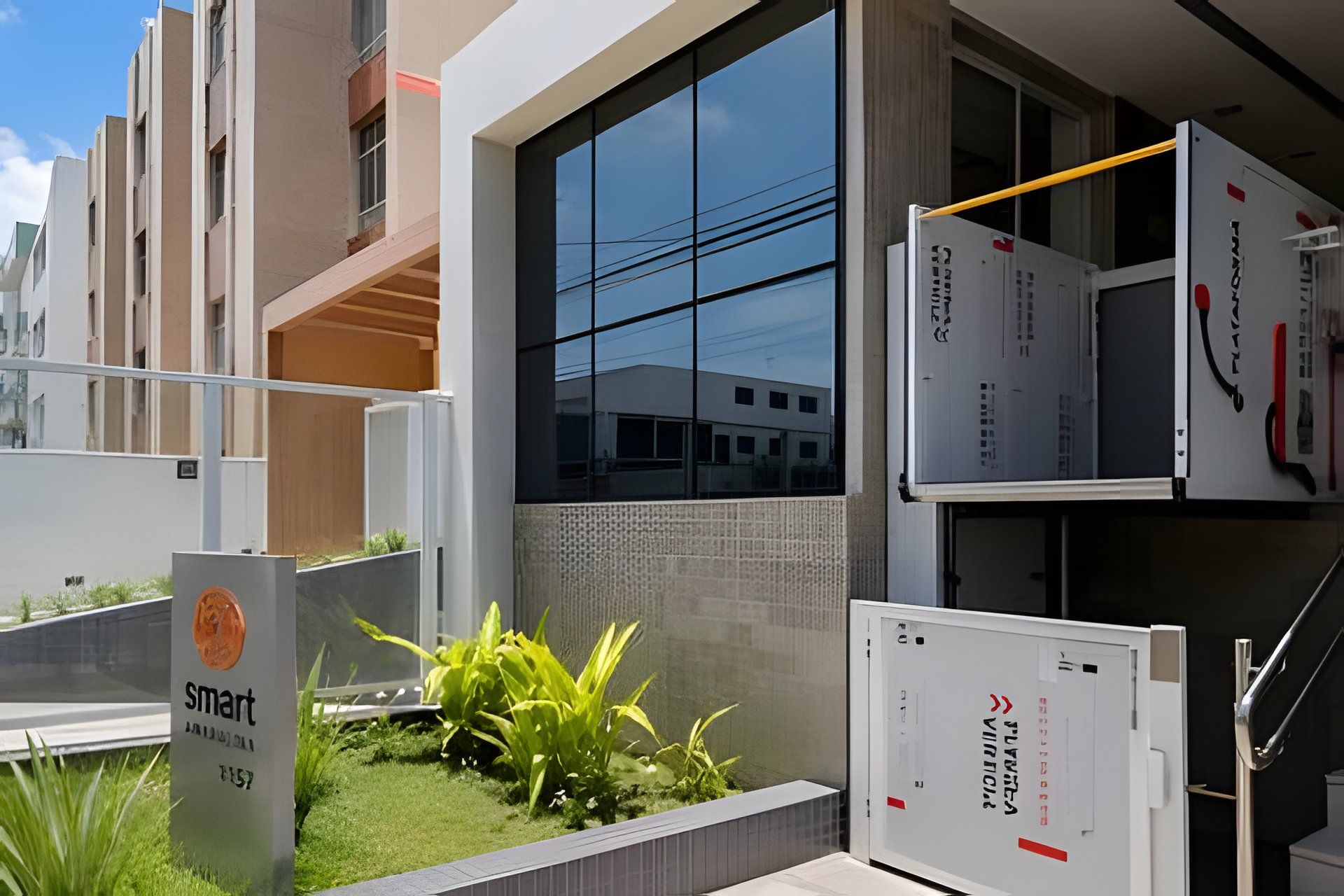 Um edifício moderno com fachada de vidro, uma placa com a inscrição 'smart' e uma estrutura metálica com detalhes em vermelho e preto.