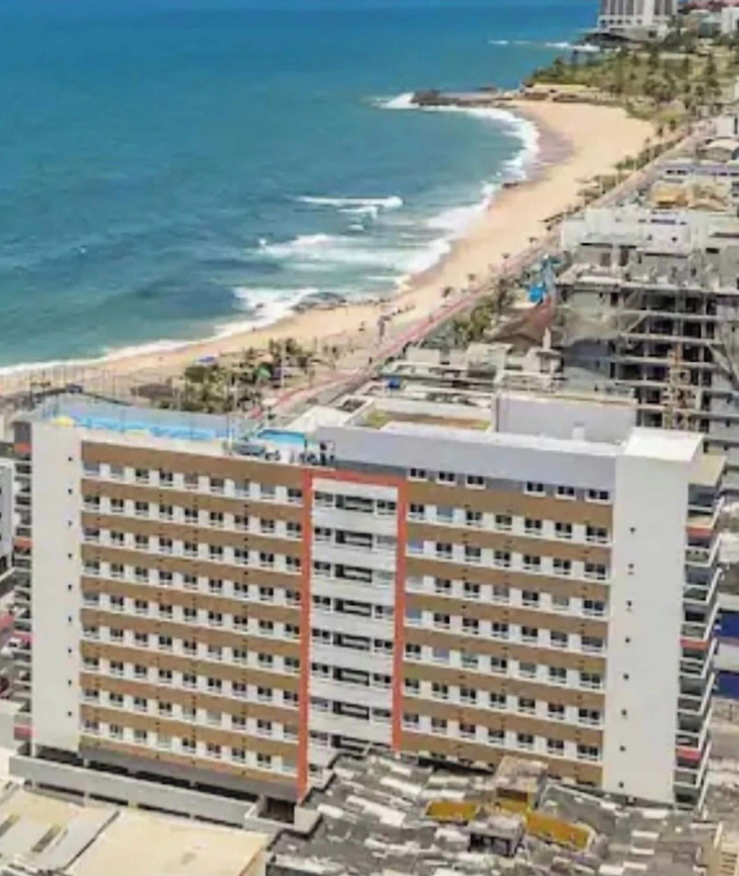Um hotel à beira-mar, com vários andares, vista para a praia e área de piscina.