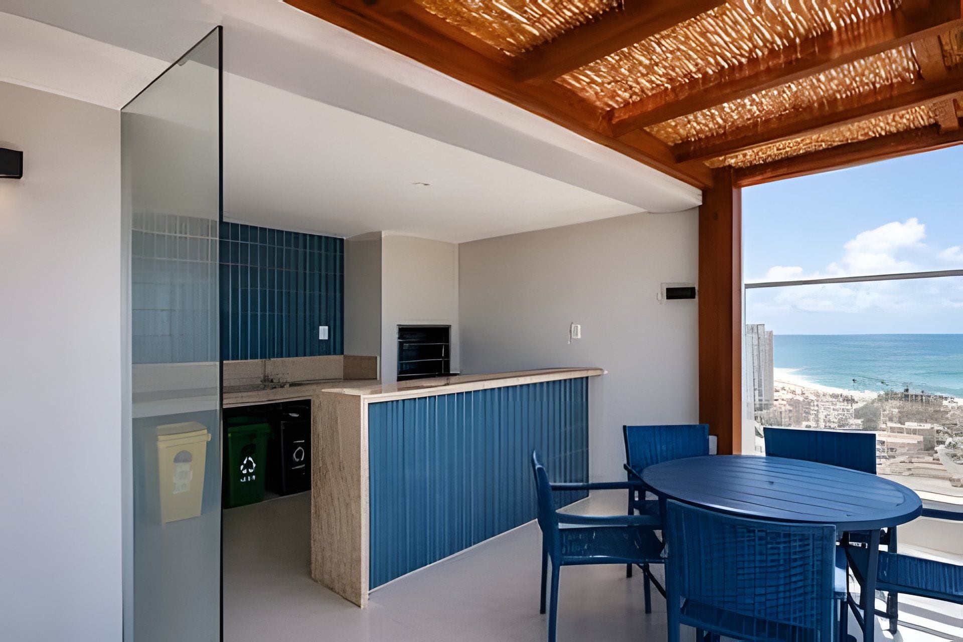 Cozinha moderna com armários azuis, divisória de vidro e vista para a praia.