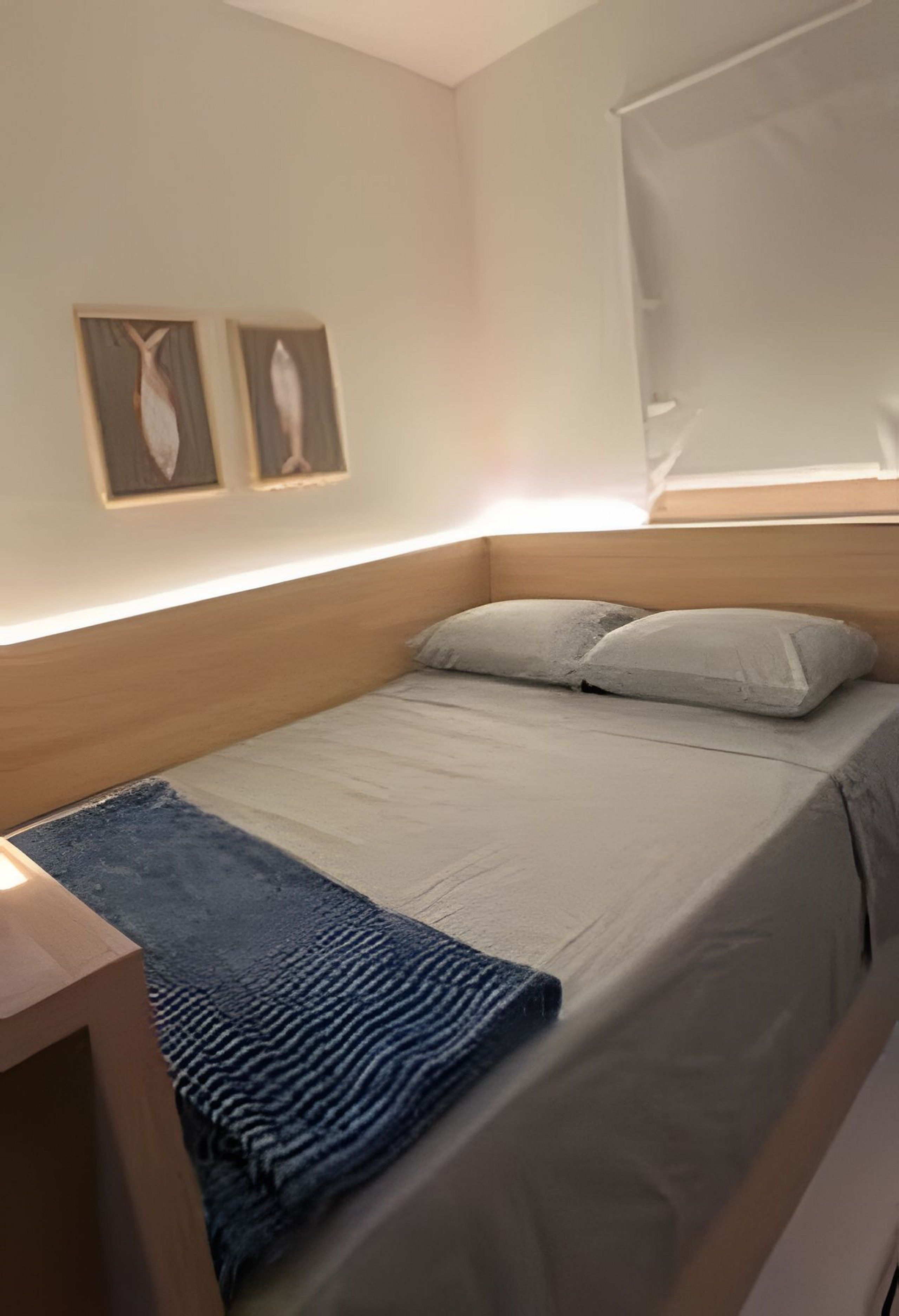 Uma cama de solteiro com cabeceira de madeira, manta azul e dois quadros pendurados na parede.