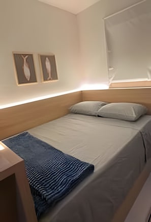 Uma cama de solteiro com cabeceira de madeira, manta azul e dois quadros pendurados na parede.