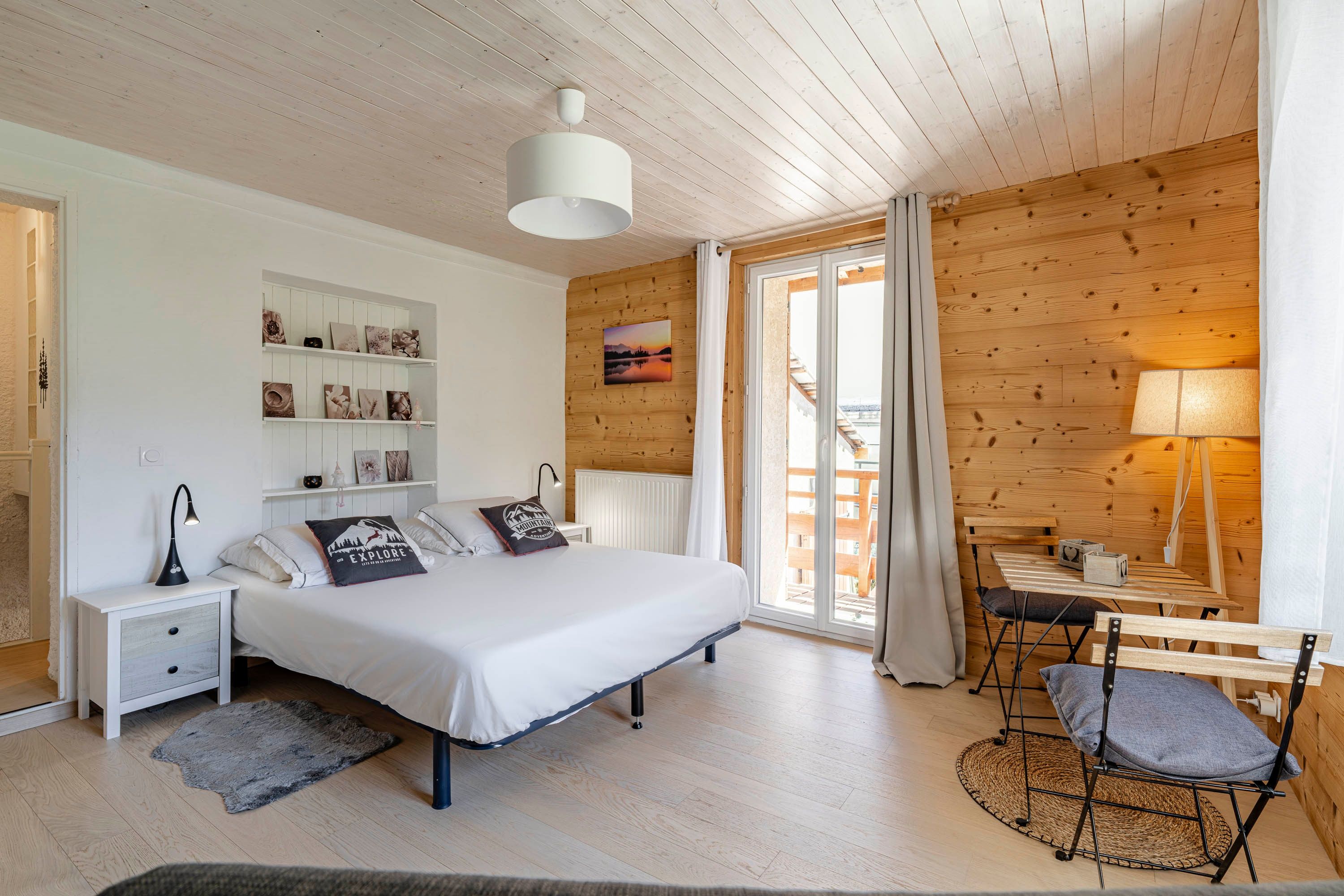 Une chambre à coucher comprenant un lit, des tables de chevet, un bureau avec une chaise, une fenêtre avec des rideaux et un mur en bois avec des étagères.