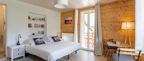 A bedroom with a bed, bedside tables, a desk with a chair, a window with curtains, and a wooden wall with shelves.