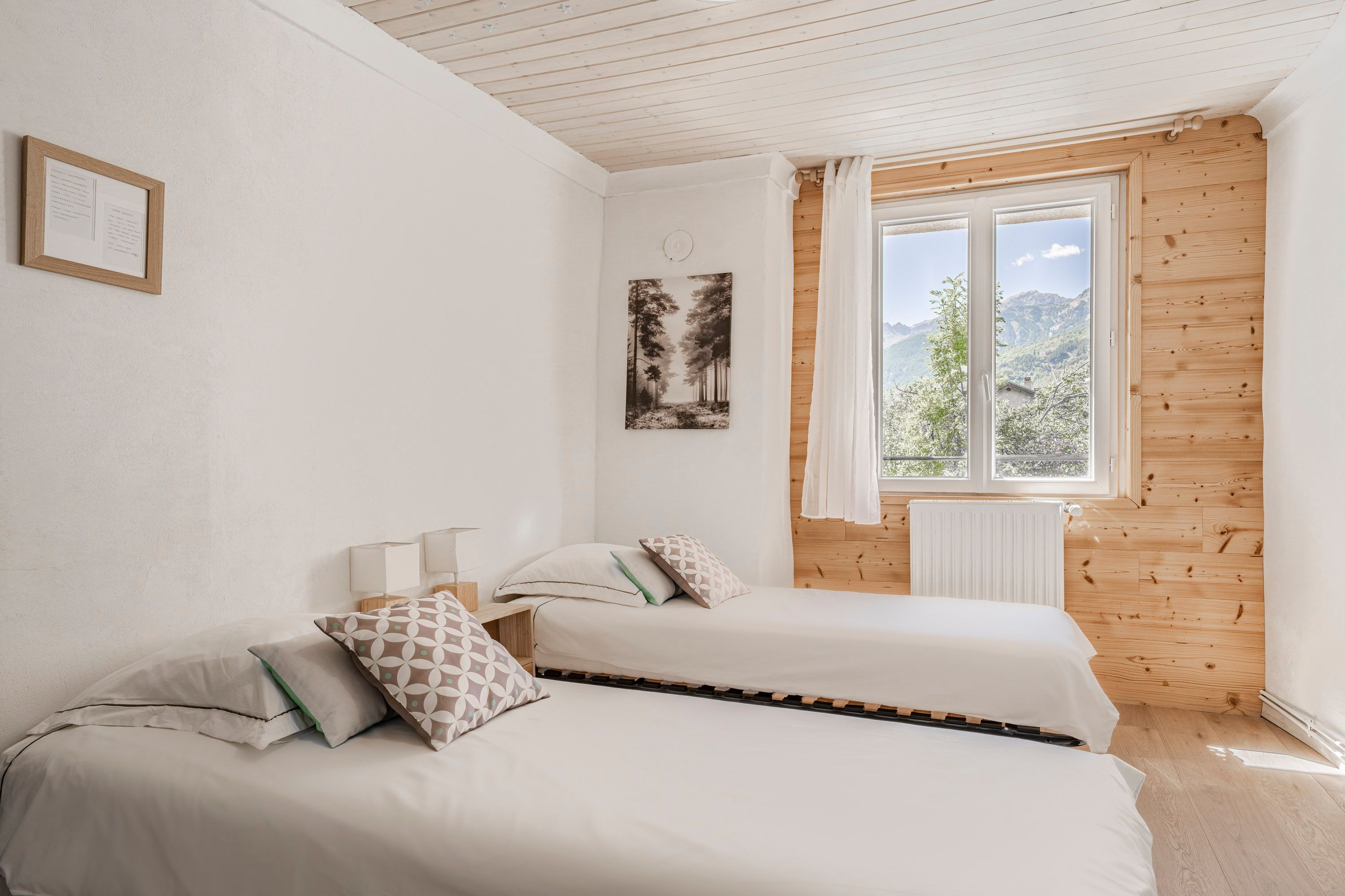A bedroom with two beds, a window with a view of mountains, and a framed picture on the wall.
