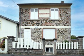 Edifici de pedra de dues plantes amb una tanca de palets blancs, una petita porta d'entrada i una placa amb un número.