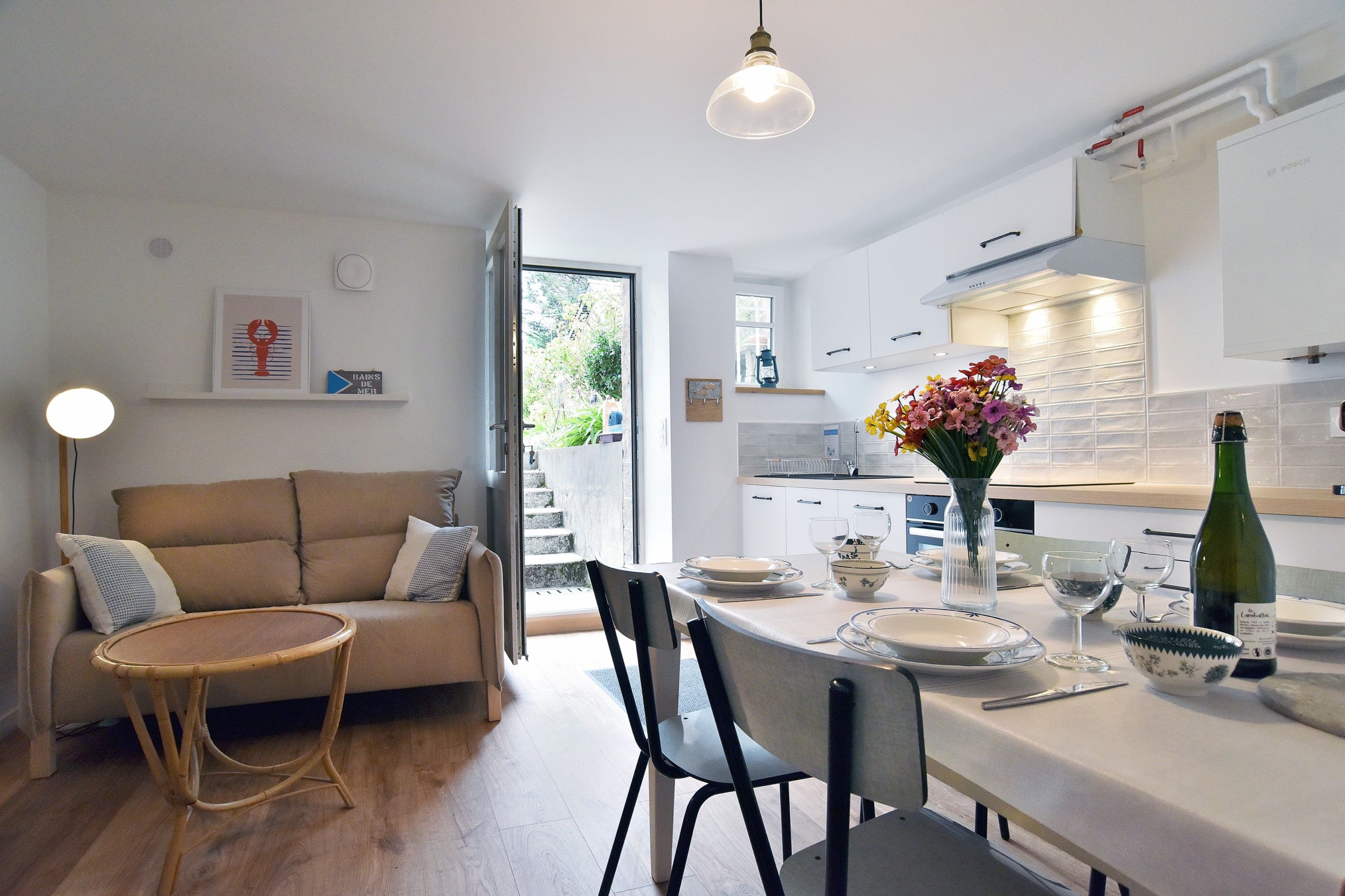 Una cocina moderna con armarios blancos, una mesa de comedor para dos personas y un florero con flores en la encimera.