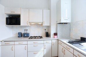 A kitchen with white cabinets, a microwave, a toaster, a gas stove, and a kettle. - Le Barthou - 500 m de la gare (Rennes)