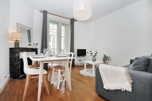 Ein modernes Wohnzimmer mit Essbereich, einem grauen Sofa und einem Fernseher auf einem Schrank.