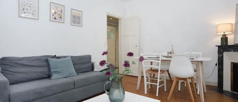 A living room with a grey sofa, a white coffee table, a dining area with a white table and chairs, and a fireplace.