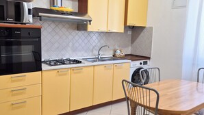 A compact kitchen with yellow cabinets, a gas stove, a microwave, and a dining area with a wooden table and metal chairs. - Vrbo Property (La Spezia)