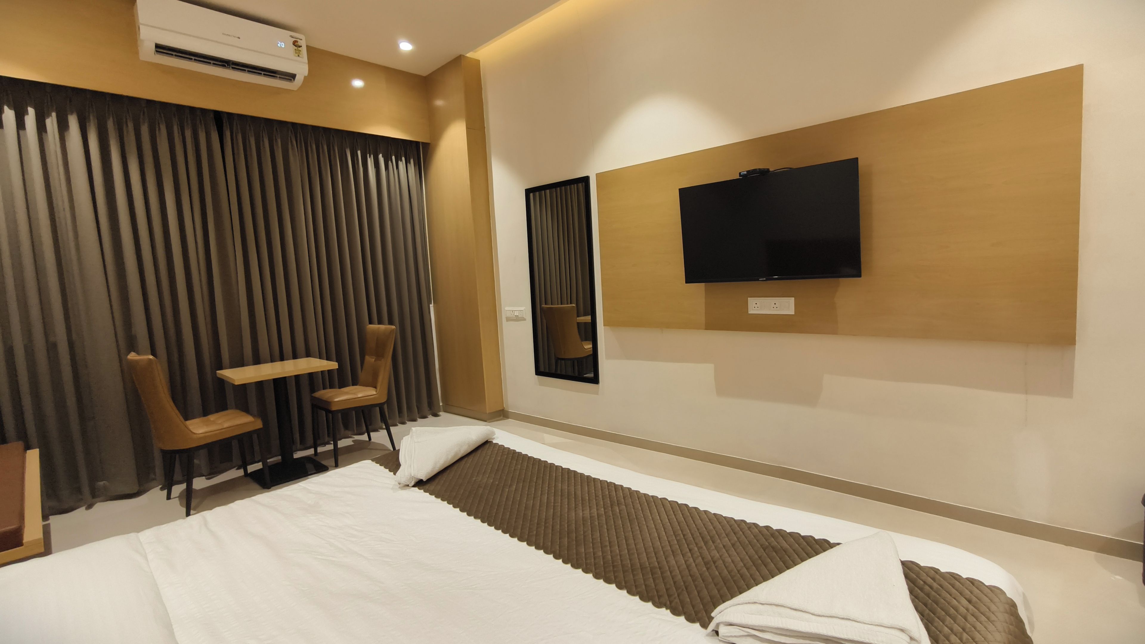 Ein Hotelzimmer mit einem Bett, einem an der Wand befestigten Fernseher, einer Sitzecke mit Sesseln und einem großen Fenster mit Vorhängen.