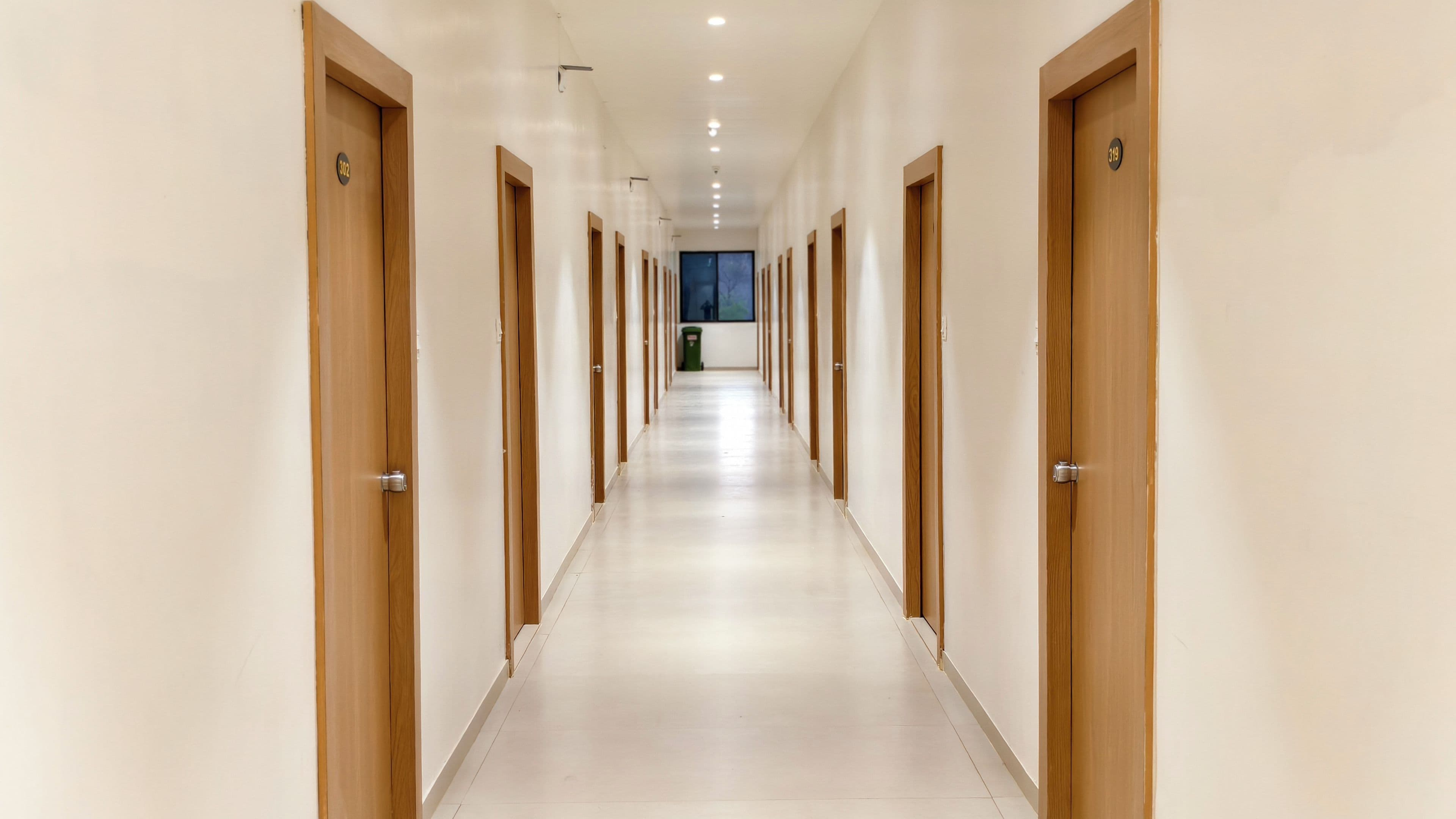A long, narrow hallway with wooden doors on both sides, leading to a window at the end.