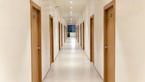 A long, narrow hallway with wooden doors on both sides, leading to a window at the end.