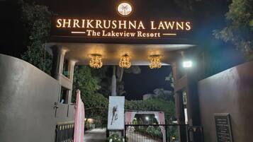 La entrada a Shrikrushna Lawns The Lakeview Resort, con un letrero sobre la puerta, candelabros y un camino que conduce al interior de la propiedad.
