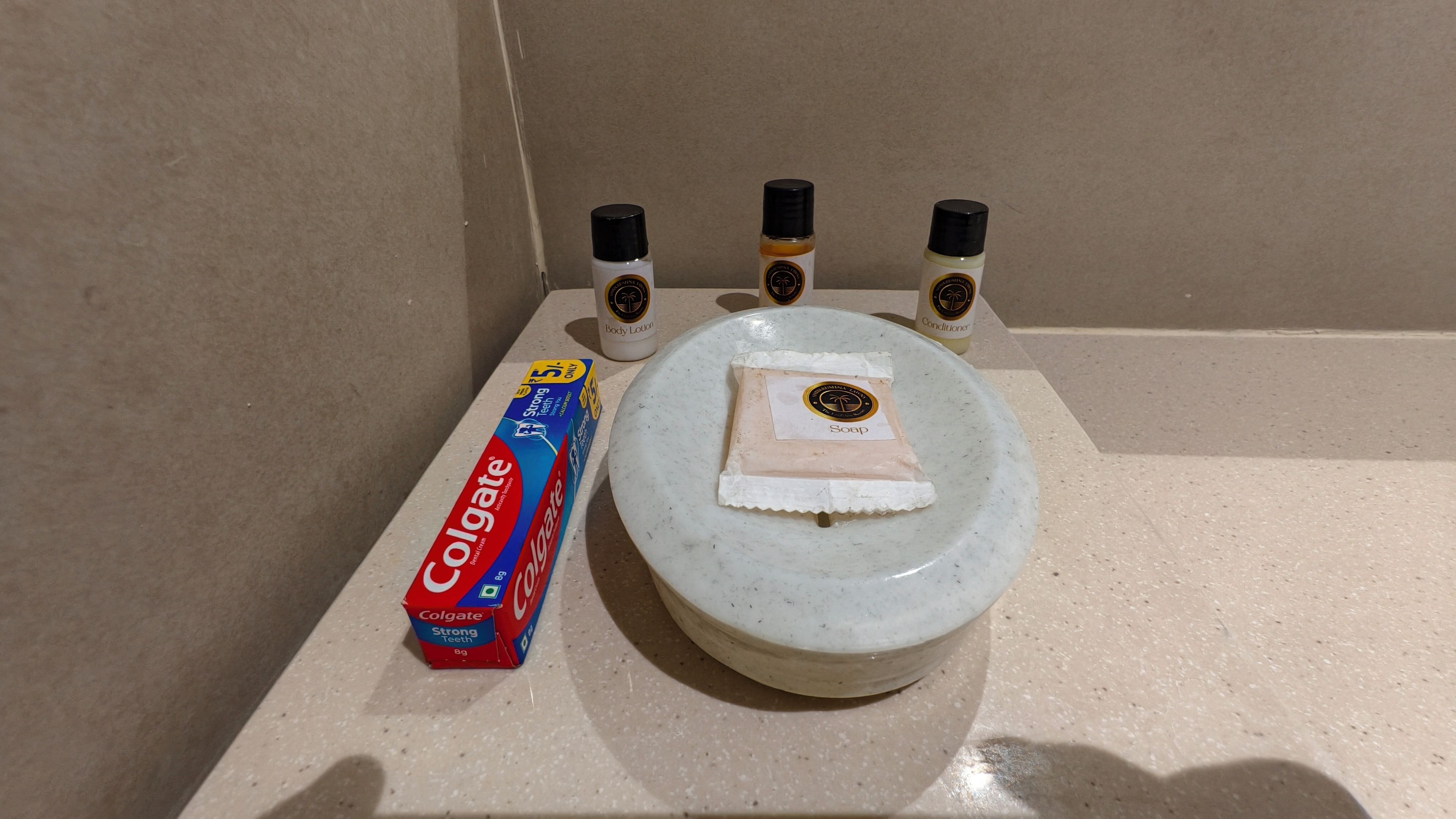 Un lavamanos con una pastilla de jabón, una caja de pasta de dientes Colgate y tres botellas de crema corporal.