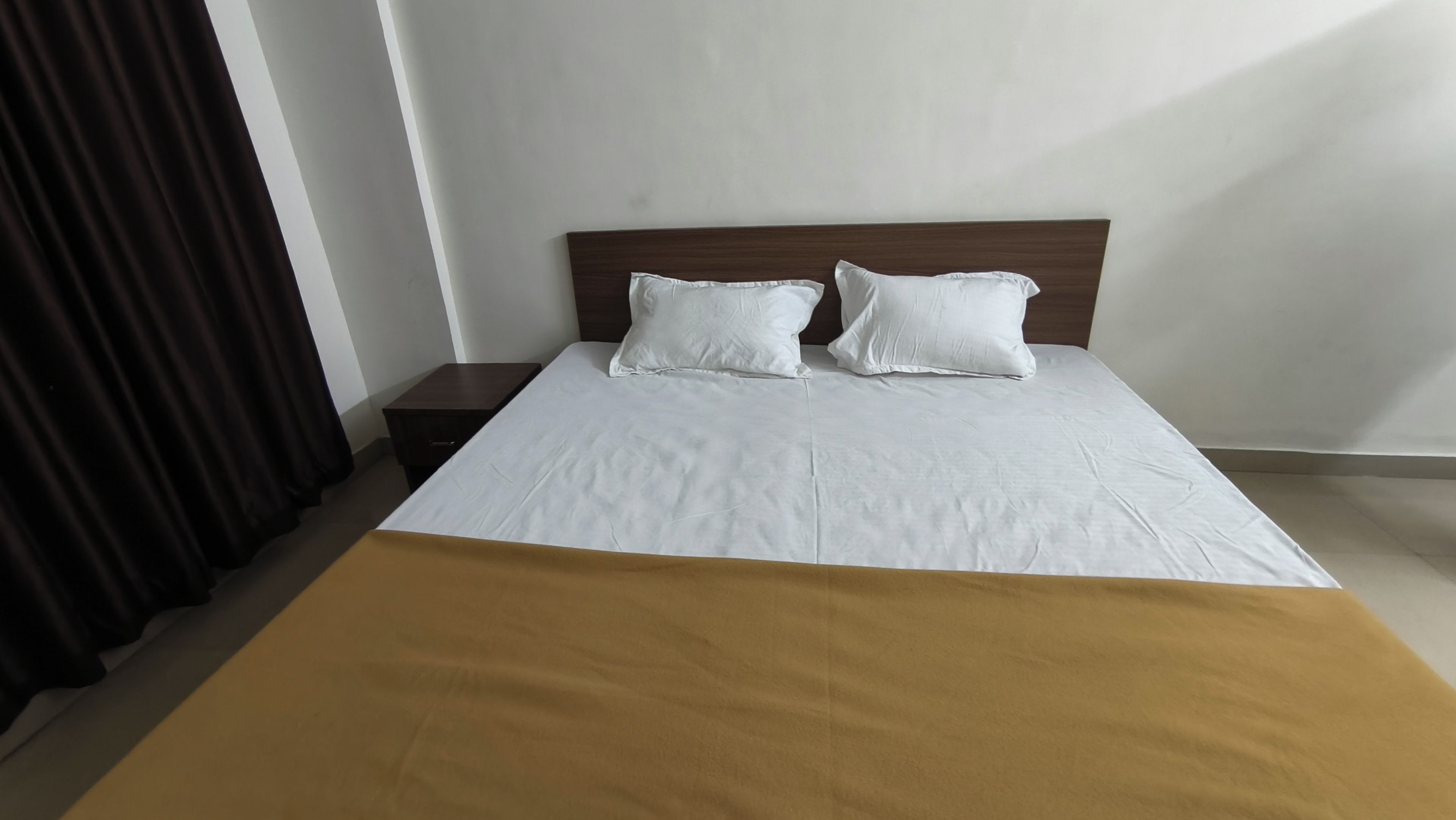 Una habitación de hotel con una cama, dos almohadas, una mesita de noche y un plaid marrón.