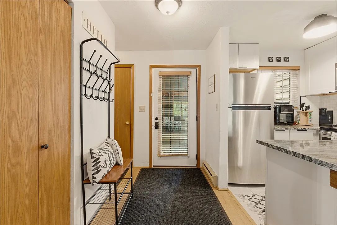 A modern kitchen with a stainless steel refrigerator, a wooden door, and a bench with a patterned cushion.