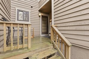 Een houten terras met een balustrade, een raam en een deur die uitkomt op een overdekte veranda.