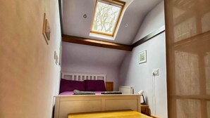 A compact room with a sloped ceiling, a skylight, a bed with a headboard, a wooden bench, and a radiator. - The Escape, beautiful country estate cottage (Y Felinheli)