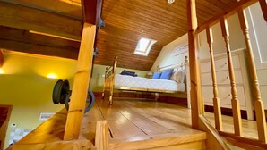 A loft bedroom with a wooden ceiling, a bed with blue bedding, and a skylight. - The Escape, beautiful country estate cottage (Y Felinheli)