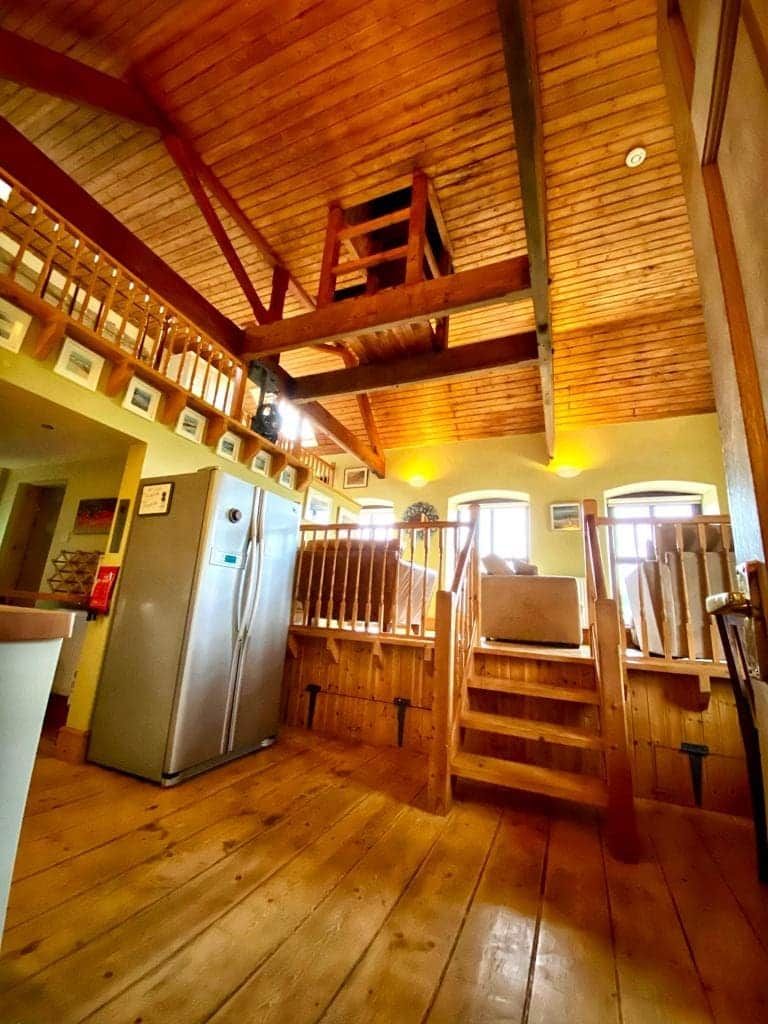A wooden interior with a staircase, a refrigerator, and a window.