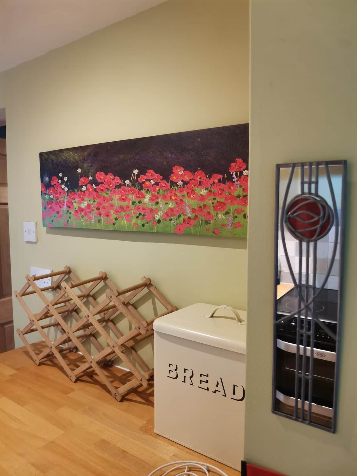 A room with a painting of flowers on the wall, a bread storage box, and a metal rack.