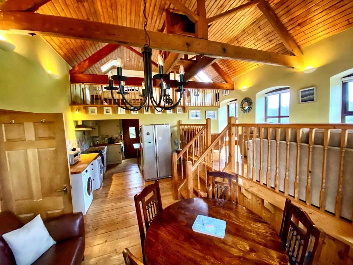 A spacious room with a wooden dining table, chairs, and a staircase leading to an upper level.