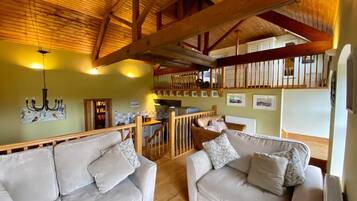 A cozy living room with two sofas, a wooden ceiling, and a kitchen area in the background.