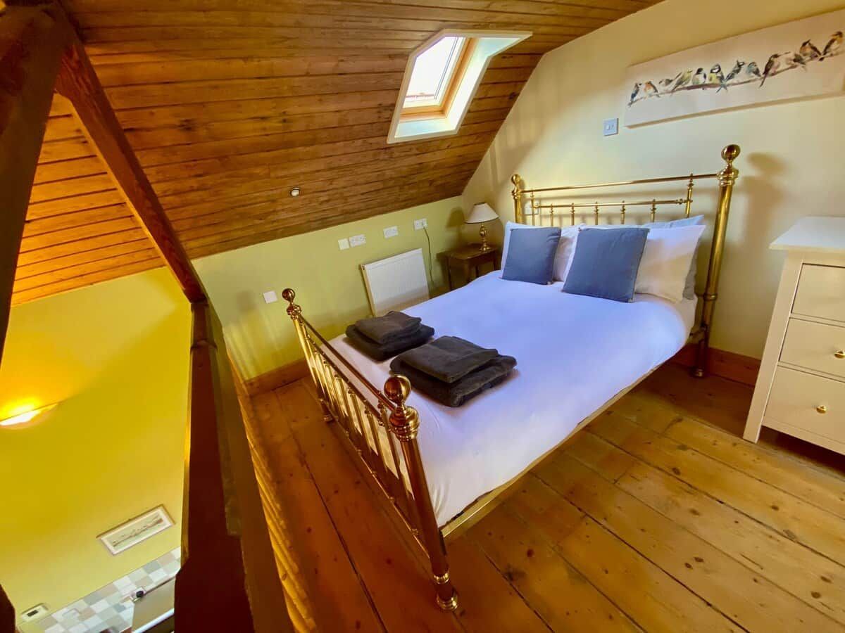 A bedroom with a wooden ceiling, a sloped roof, a bed with pillows, a bedside table, and a wall-mounted shelf with bird decorations.