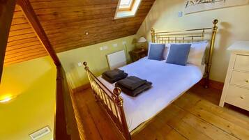 A bedroom with a wooden ceiling, a sloped roof, a bed with pillows, a bedside table, and a wall-mounted shelf with bird decorations.
