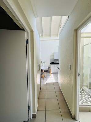 A narrow hallway leading to a kitchen area with a dining table and chairs. - Luxury High-end Modern Luxe Apartment (Johannesburg)