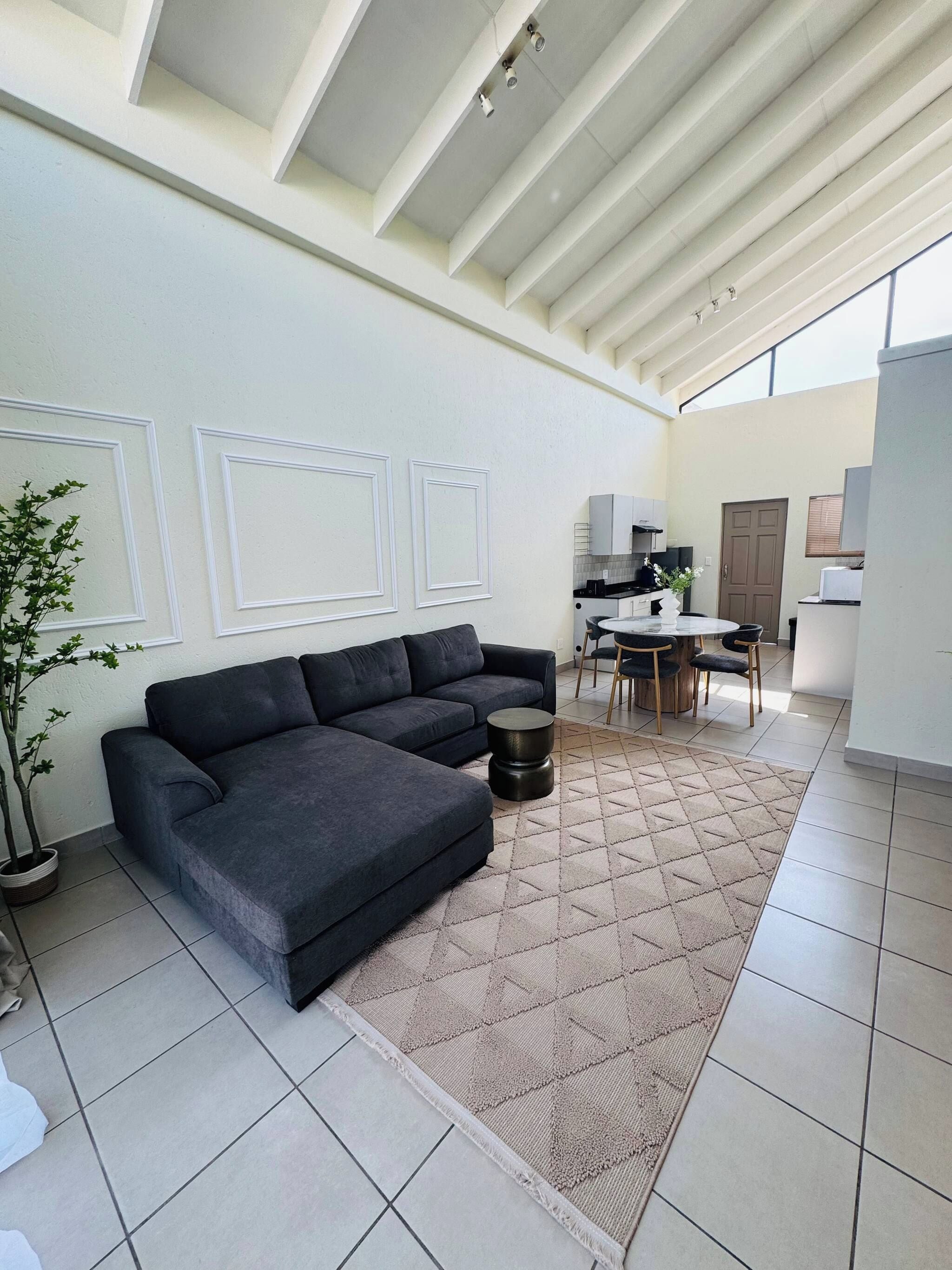A modern living room with a sectional sofa, a dining area with a table and chairs, and a kitchen in the background.