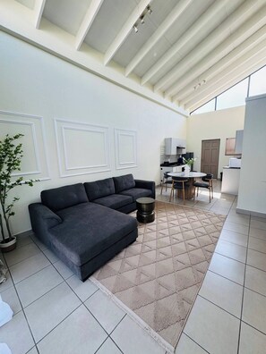 Ein modernes Wohnzimmer mit einer Eckcouch, einem Essbereich mit Tisch und Stühlen sowie einer Küche im Hintergrund.