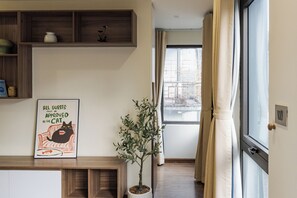 A living room with a wooden cabinet, a potted plant, a framed picture, and a window with curtains. - Spacious 2-bedroom apartment in Hoan Kiem (Hà Nội)