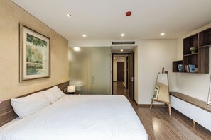 Una camera d'albergo con un letto grande, un quadro appeso al muro, un comodino con una lampada, un pavimento in legno e un piccolo cavalletto con uno specchio.