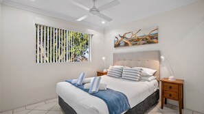A bedroom with a bed, a ceiling fan, a window with blinds, a painting, and bedside tables. - Sanctuary Lake Apartment 67 - Beachside Oasis in Currumbin - Min. 3 Night Stays - Linen Provided (Currumbin)