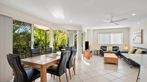 A spacious living area with a dining table, sofas, and a ceiling fan. - Sanctuary Lake Apartment 67 - Beachside Oasis in Currumbin - Min. 3 Night Stays - Linen Provided (Currumbin)