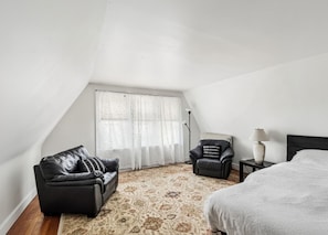 A bedroom with a black leather sofa, a patterned rug, a white bed, and a floor lamp.