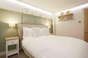 Ein Schlafzimmer mit einem großen Bett, Nachttischen und einem Wandregal mit Kleiderhaken.
