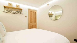 Une chambre à coucher avec un lit, une porte en bois, un miroir fixé au mur et une étagère avec des cintres.