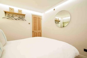 Ein Schlafzimmer mit einem Bett, einer Holztür, einem an der Wand befestigten Spiegel und einem Regal mit Kleiderhaken.
