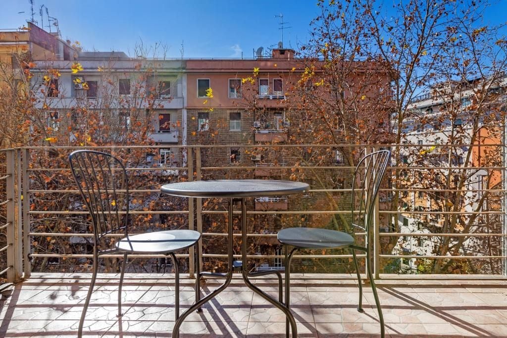 A terrace with a round table and two chairs, overlooking a residential area with buildings and trees.