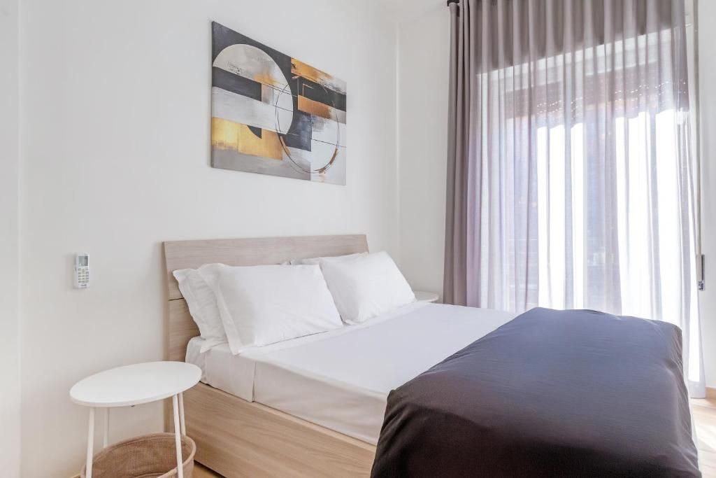 A modern bedroom with a bed, a bedside table, a wall-mounted phone, and a window with curtains.