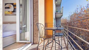 A balcony with a table and chairs, a bed, and a view of autumn trees.